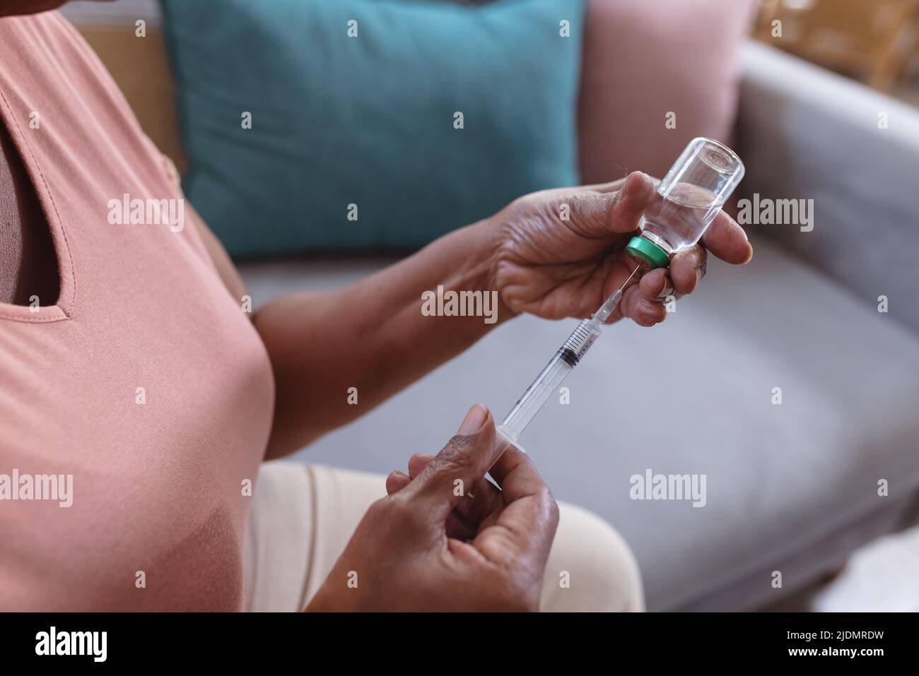 Midsection of african american senior woman holding vial and syringe while sitting on sofa at home Stock Photo