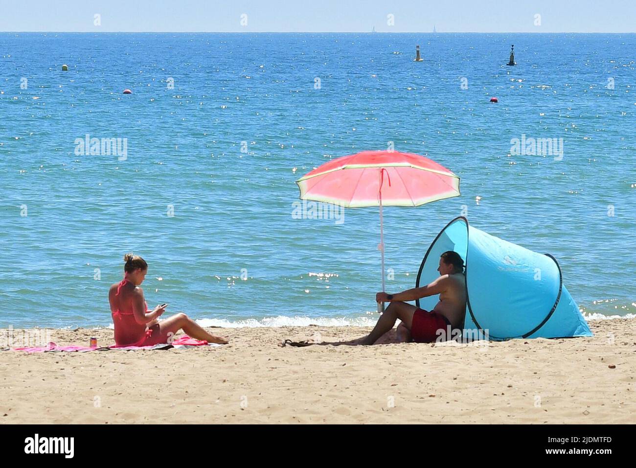 Boscombe, Bournemouth, Dorset, UK, 22nd June 2022, Weather. Hot afternoon in glorious summer sunshine. Couple sitting on the beach with red sun umbrella. Credit: Paul Biggins/Alamy Live News Stock Photo