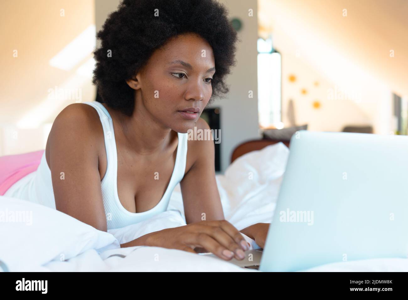 African american young afro woman using laptop while lying on bed in ...