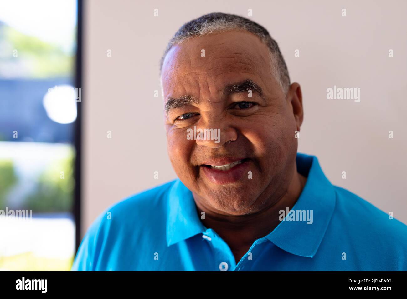 Close-up portrait of smiling biracial senior man against white wall in retirement home, copy space Stock Photo