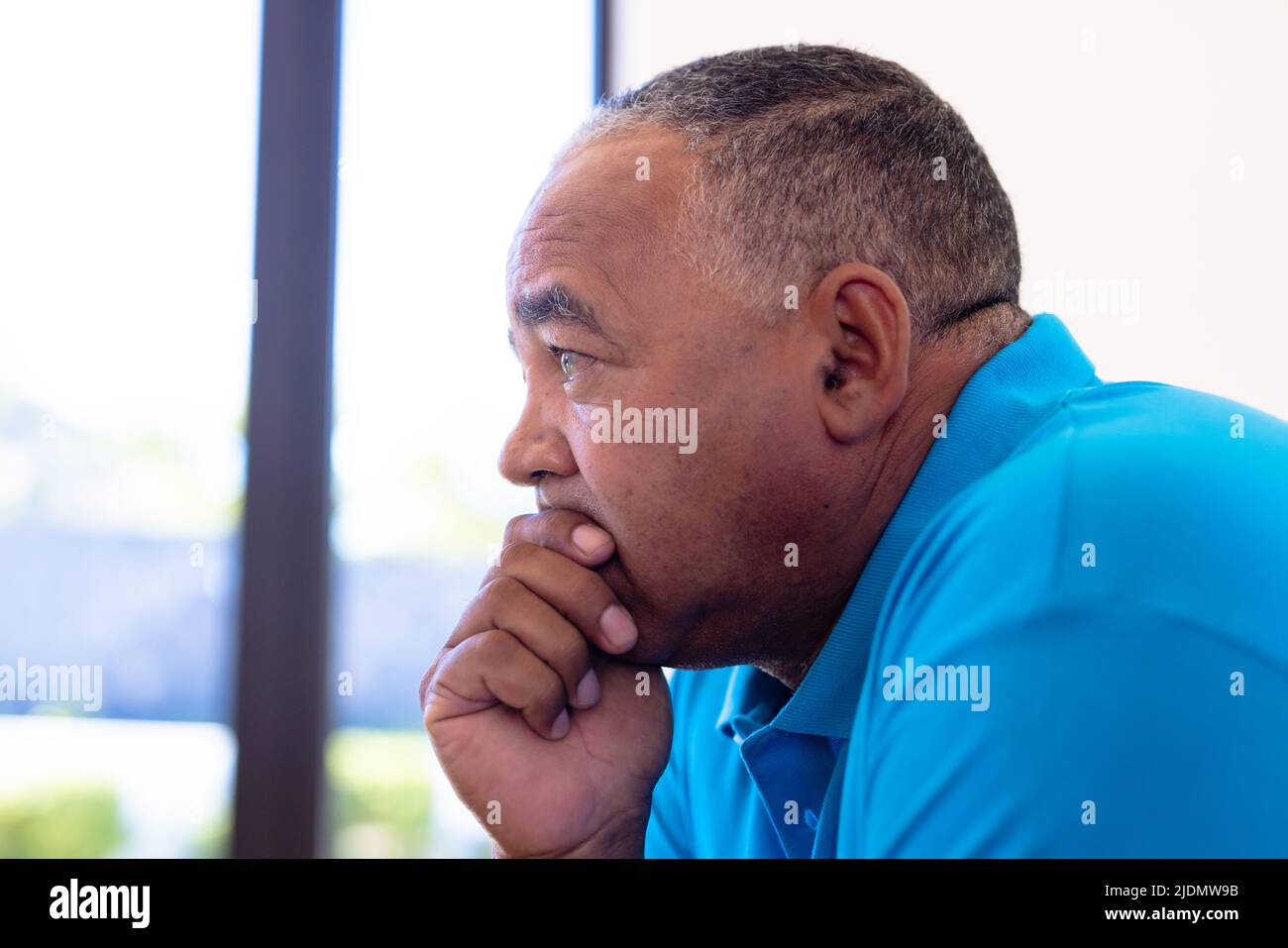 Side view of thoughtful biracial senior man with hand on chin looking away in retirement home Stock Photo