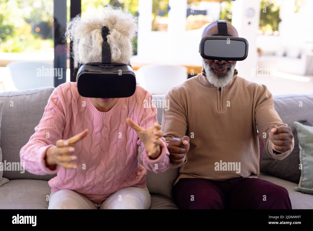 Multiracial excited senior friends enjoying virtual reality simulators on sofa in retirement home Stock Photo