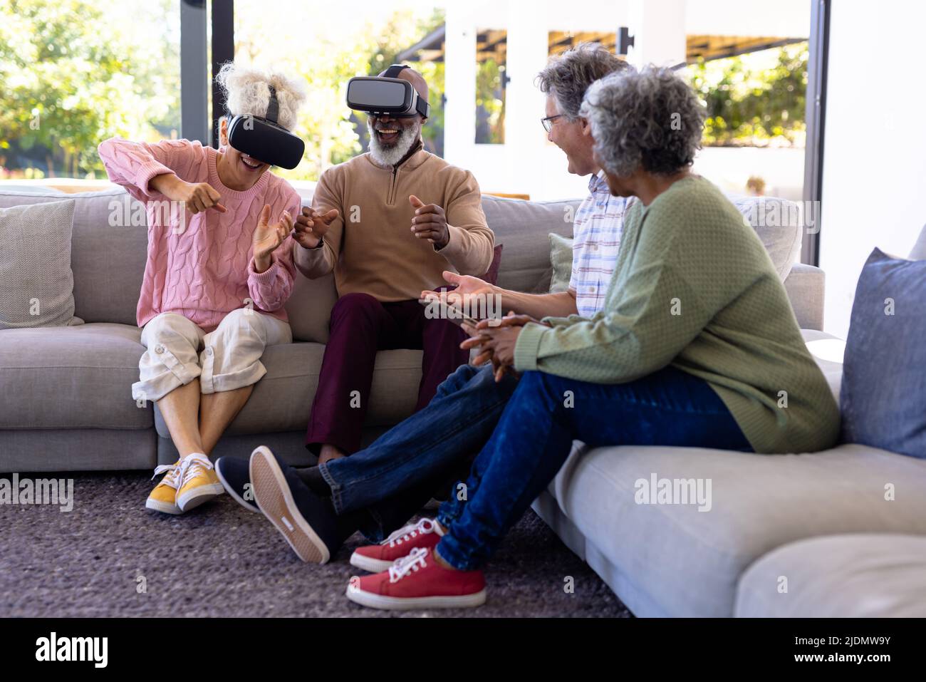Multiracial seniors looking at cheerful friends gesturing while using virtual reality simulators Stock Photo