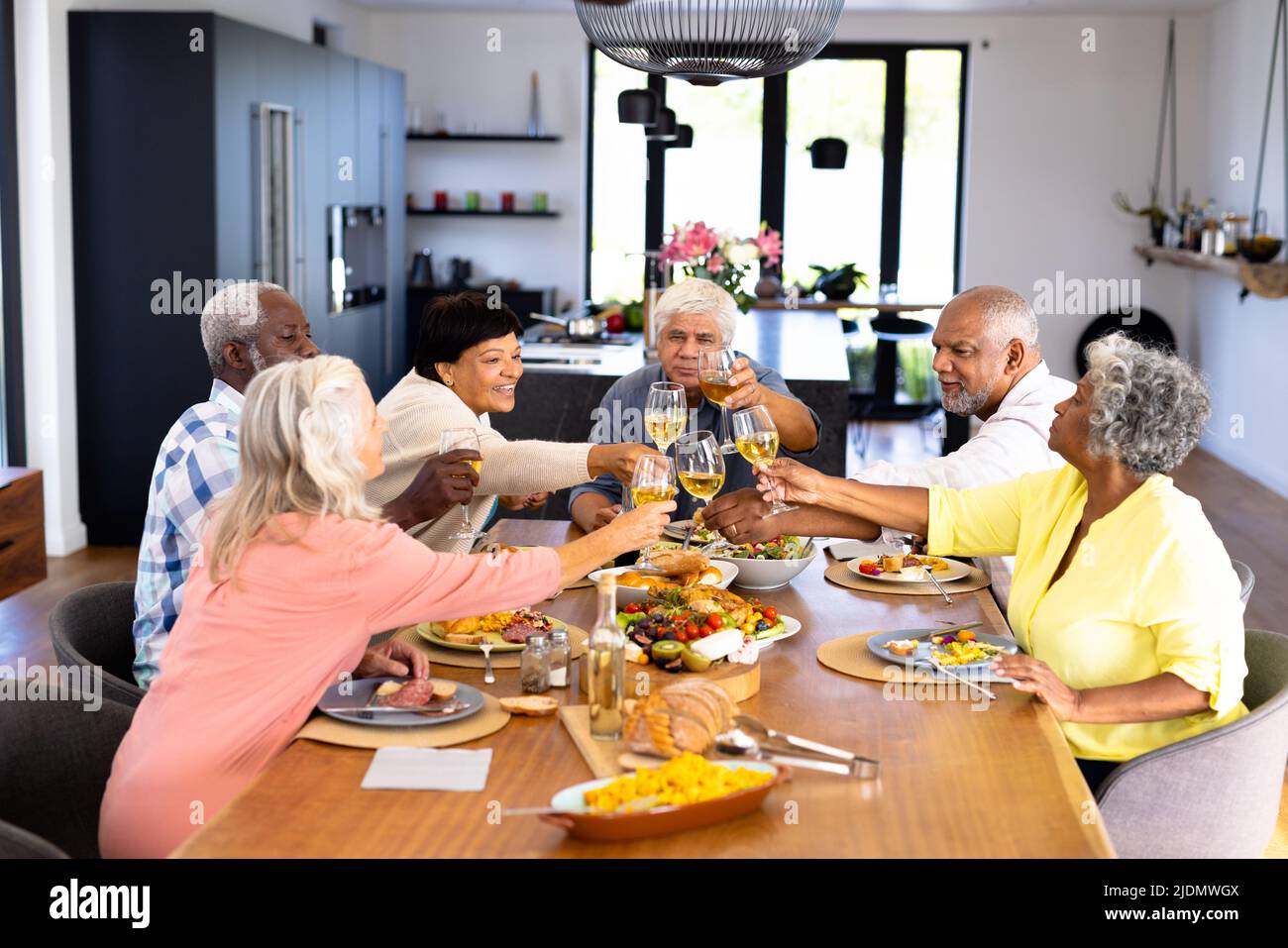 Happy multiracial senior friends toasting wineglasses while having lunch at dining table Stock Photo
