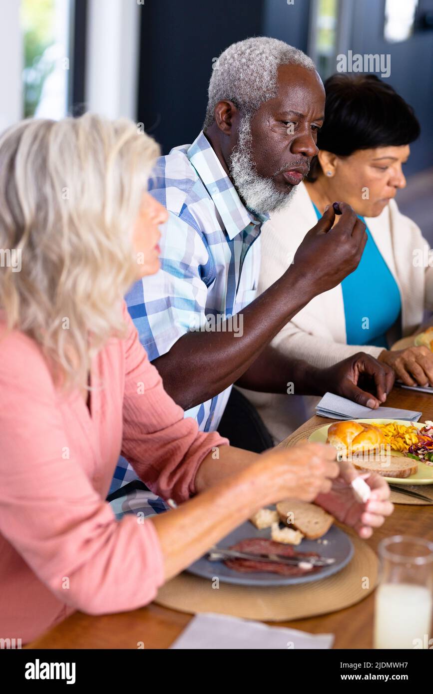 African american senior man eating lunch with multiracial female friends at dining table Stock Photo