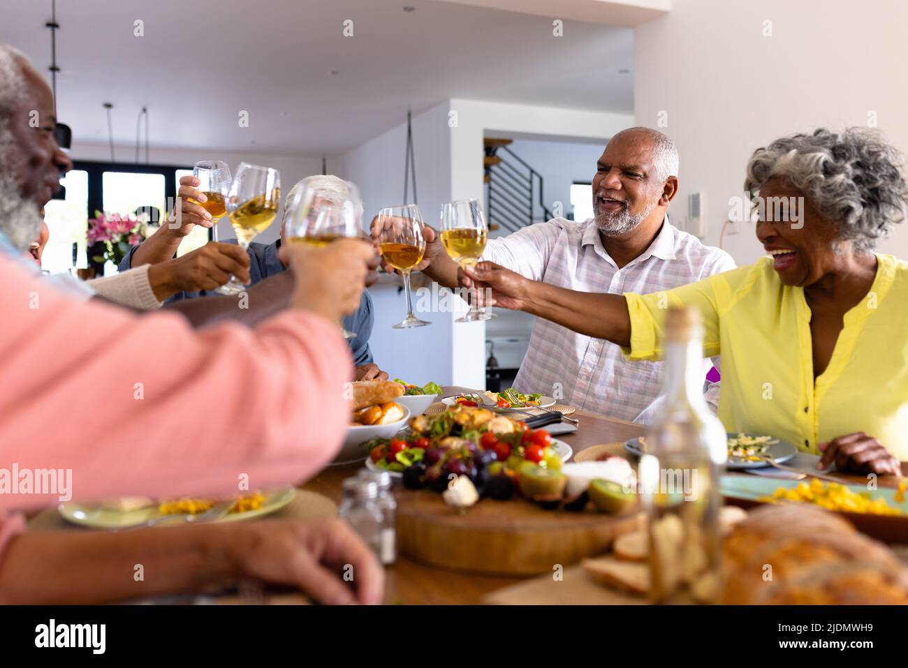 Cheerful multiracial senior friends toasting wine while having lunch at dining table in nursing home Stock Photo