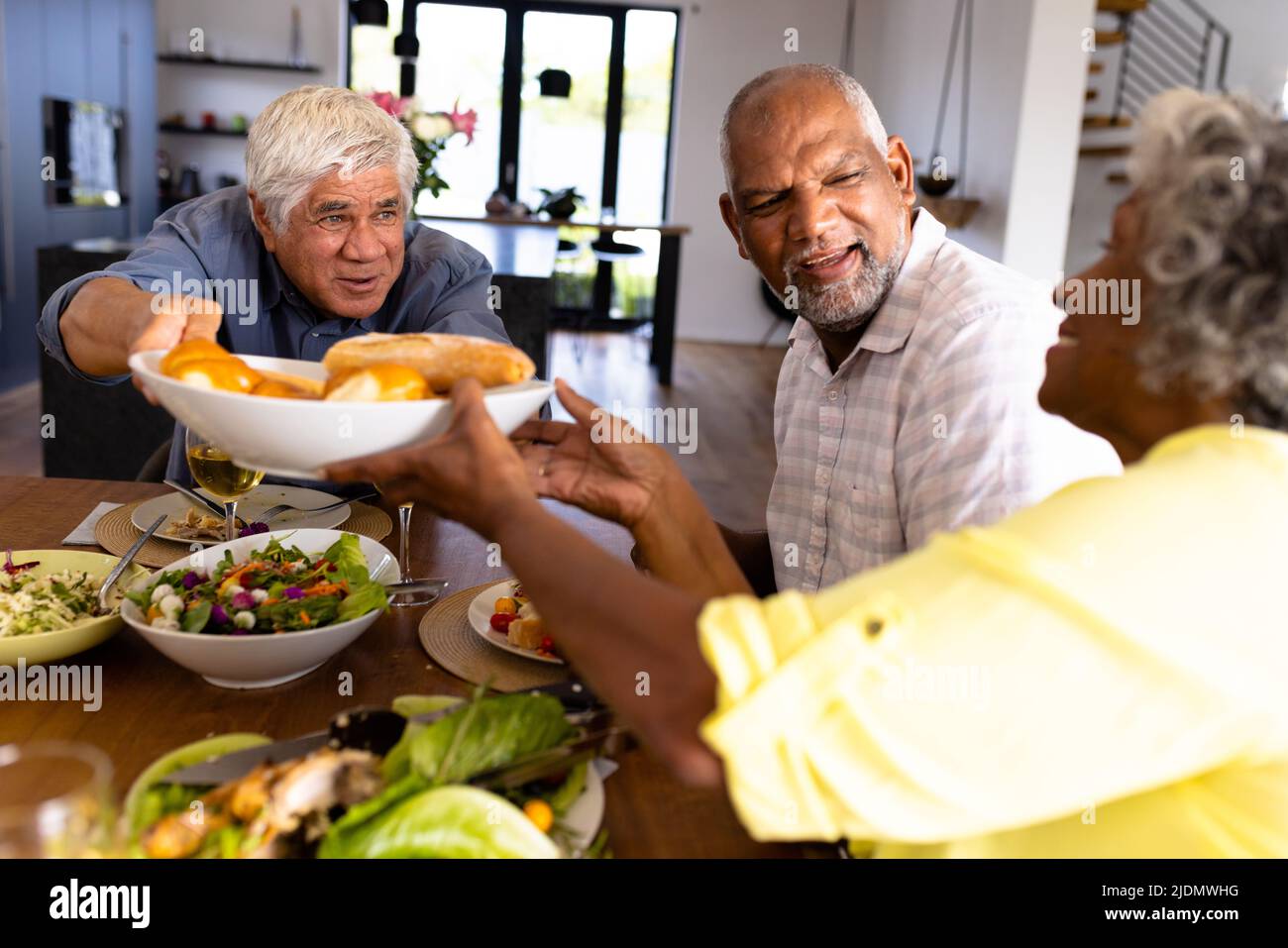 Smiling biracial senior man giving bread to woman while having lunch at dining table in nursing home Stock Photo