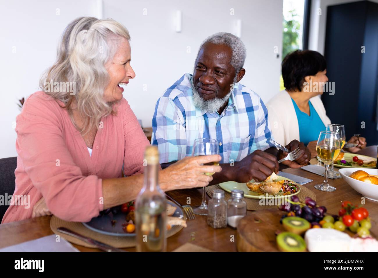 Happy multiracial senior friends talking while having lunch at dining table in nursing home Stock Photo