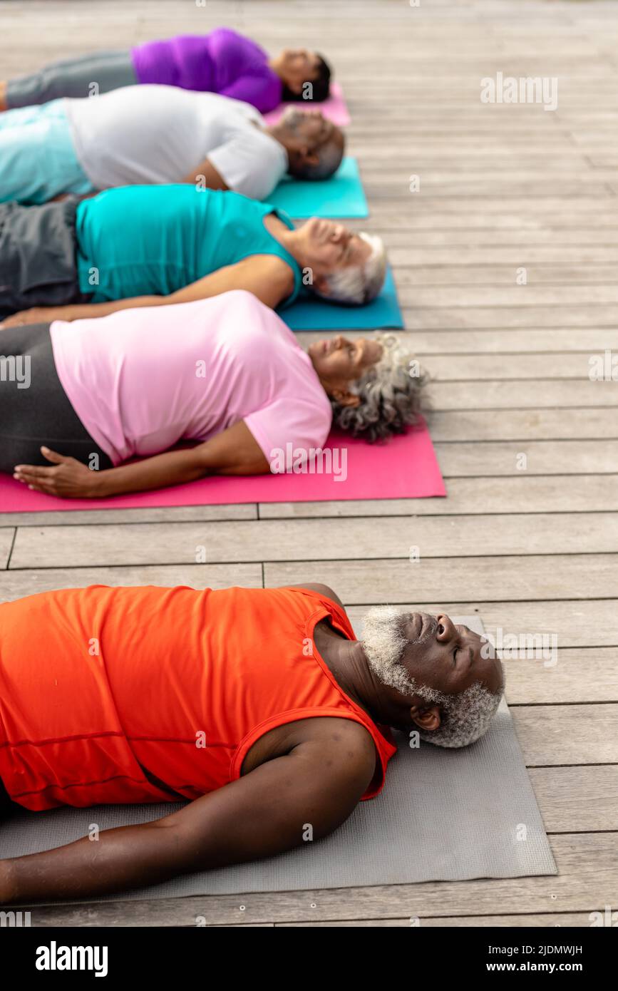 Multiracial senior friends with eyes closed exercising while lying on mats over hardwood floor Stock Photo