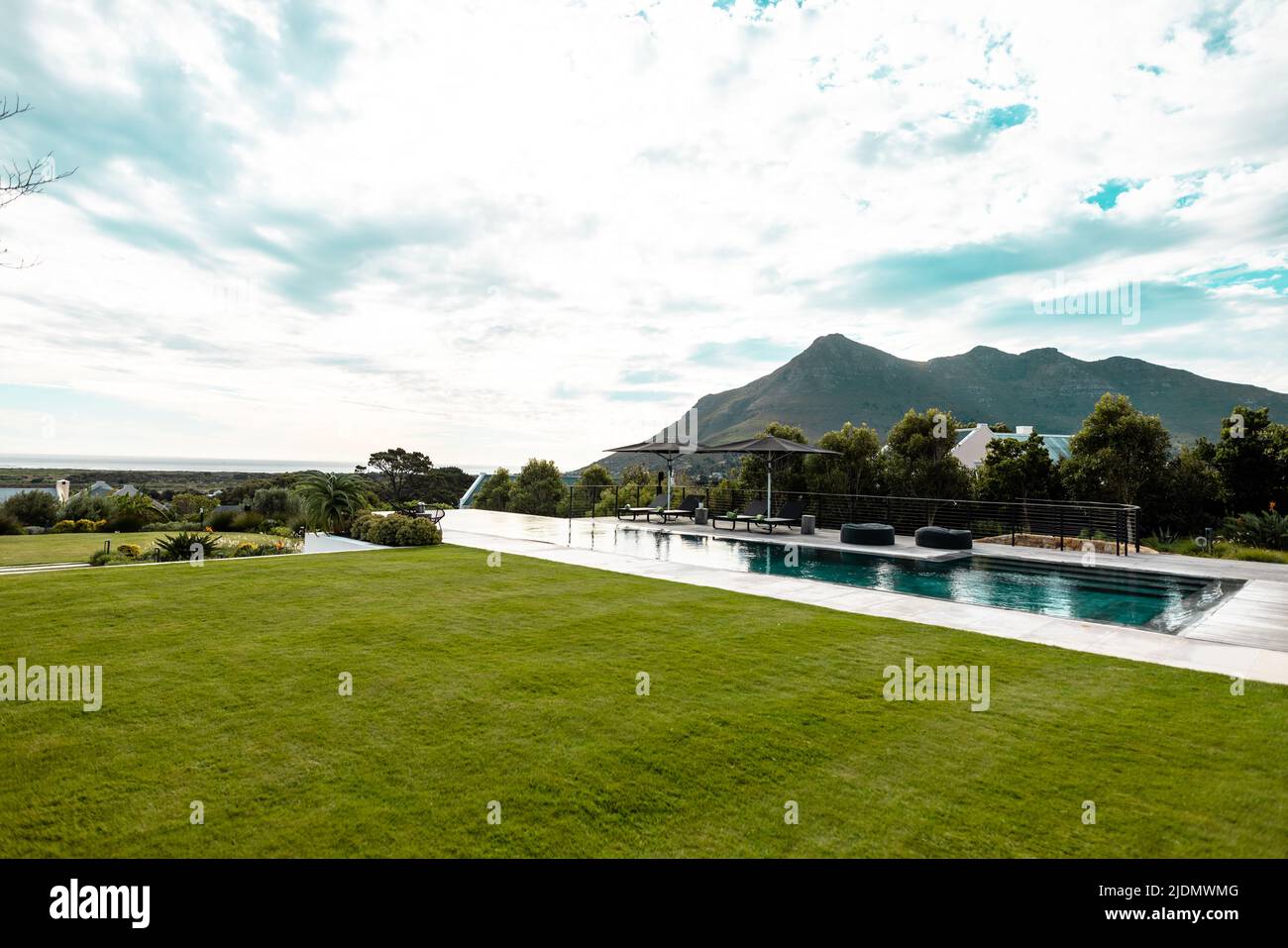 Scenic view of grassy land and swimming pool against mountain and cloudy sky Stock Photo
