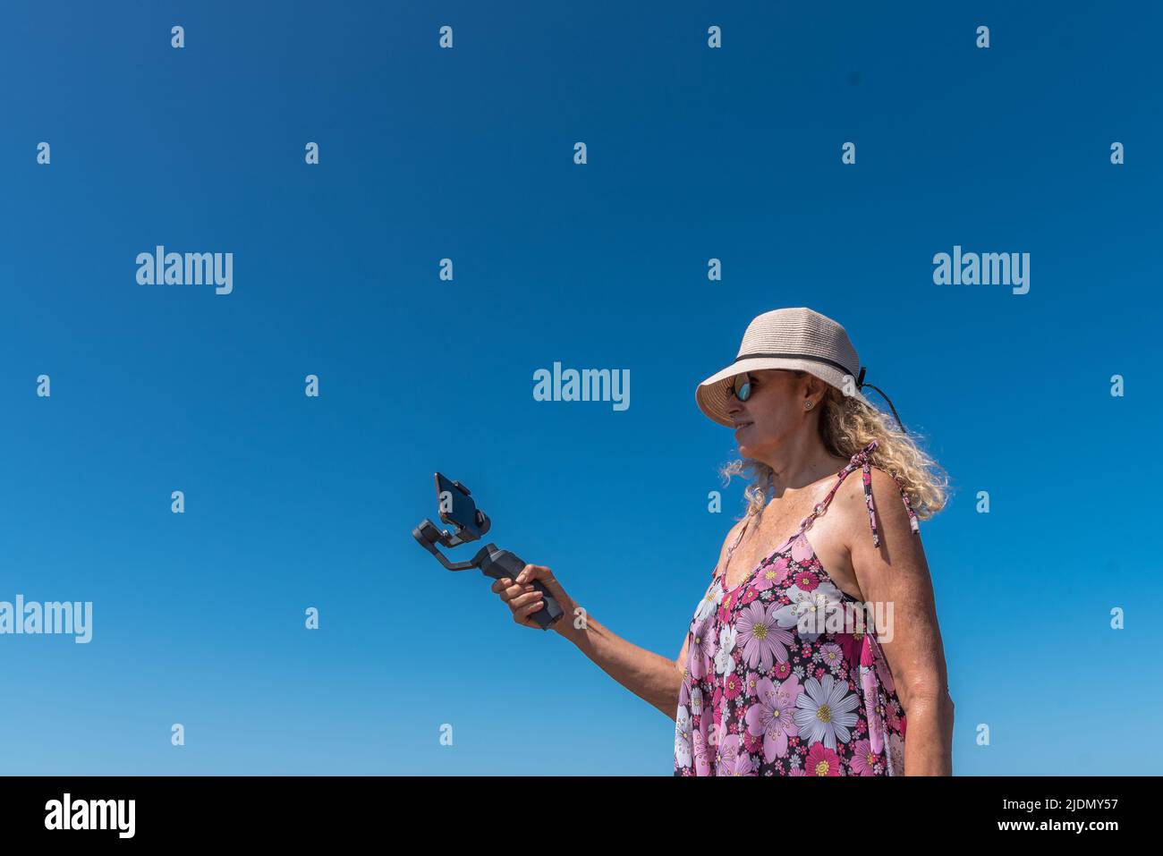 Low angle view of a woman recording with a mobile outdoors with the blue sky in the background Stock Photo