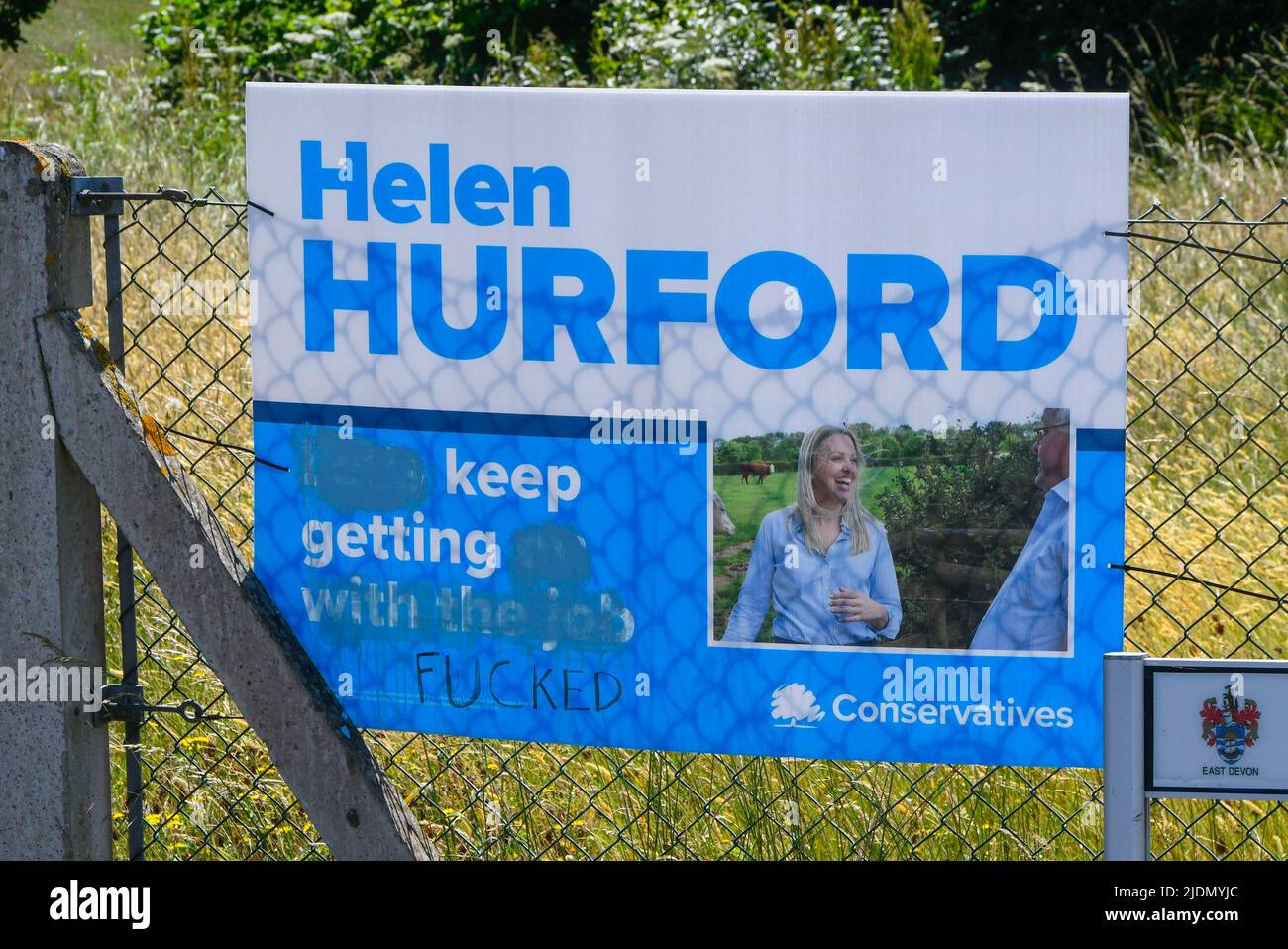 Axminster, Devon, UK.  22nd June 2022.  Election poster which has been defaced with a rude word to change the meaning of the slogan for the Conservatives candidate Helen Hurford at Axminster in Devon ahead of tomorrows parliamentary election for the Tiverton and Honiton constituency.  Picture Credit: Graham Hunt/Alamy Live News Stock Photo