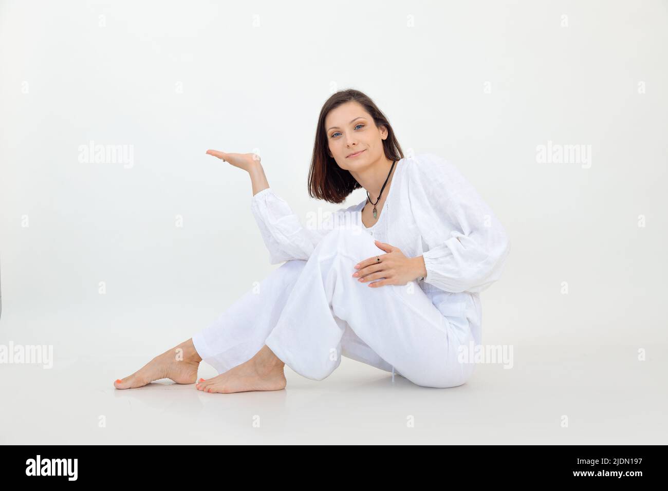 Attractive smiling and charming brunette woman sit on white background. Showing something imaginary by hands. Copy space Stock Photo