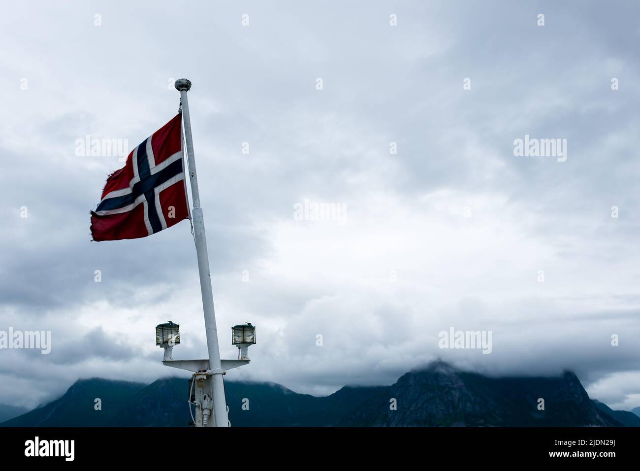 Norwegian flag waving on board a ship in Norwegian sea, Atlantic ocean with cloud covered mountains in the background Stock Photo