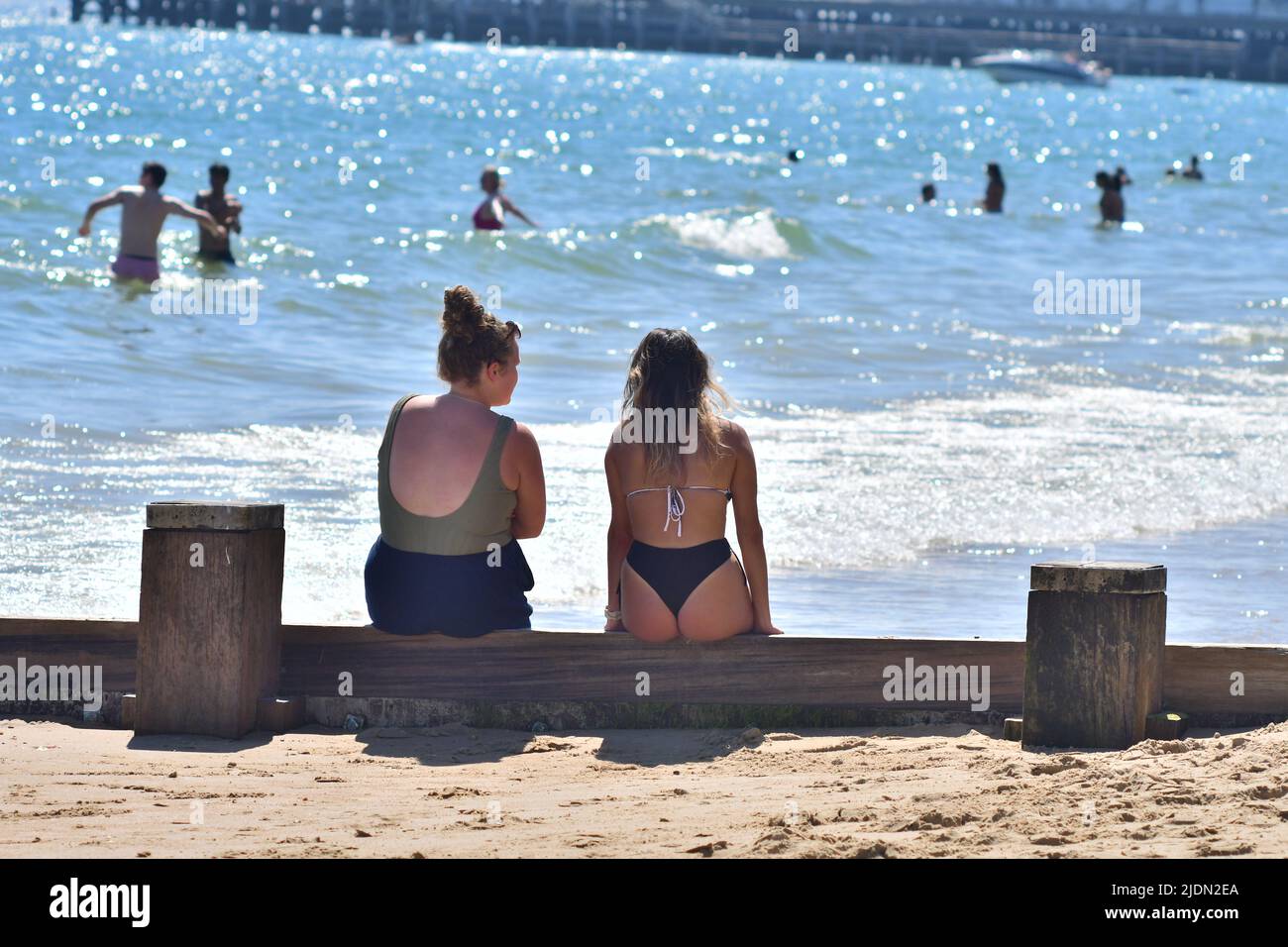 Bournemouth, Dorset, UK, 22nd June 2022, Weather. Hot afternoon in glorious summer sunshine. Two girls sitting on a groyne (wave breaker). Credit: Paul Biggins/Alamy Live News Stock Photo