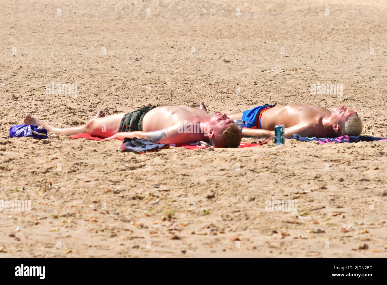 Bournemouth, Dorset, UK, 22nd June 2022, Weather. Hot afternoon in glorious summer sunshine. Two men lying down sunbathing on the beach. Credit: Paul Biggins/Alamy Live News Stock Photo