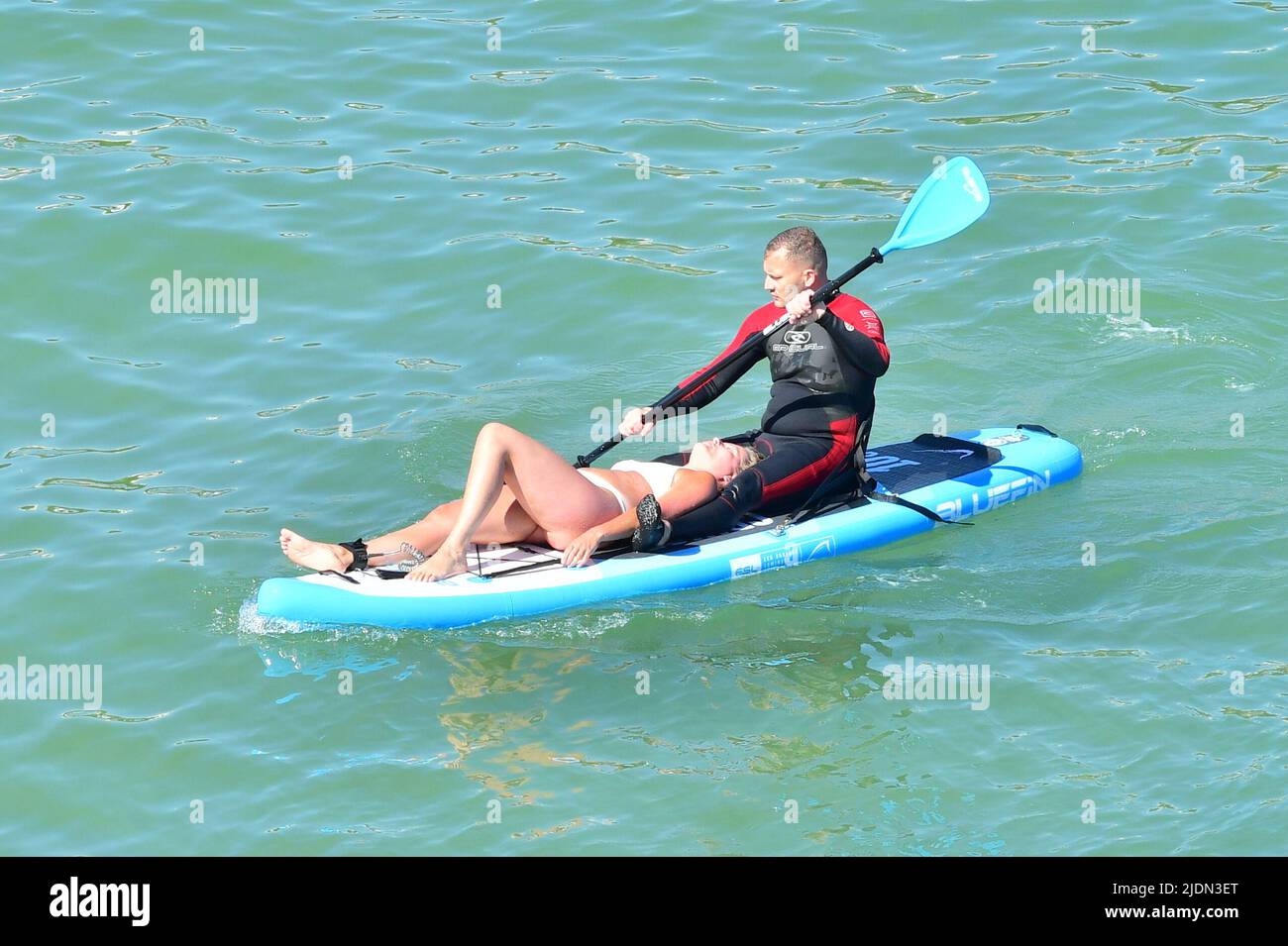 Bournemouth, Dorset, UK, 22nd June 2022, Weather. Hot afternoon in glorious summer sunshine. Woman in bikini lying on paddleboard while a man in a wetsuit paddles. Credit: Paul Biggins/Alamy Live News Stock Photo