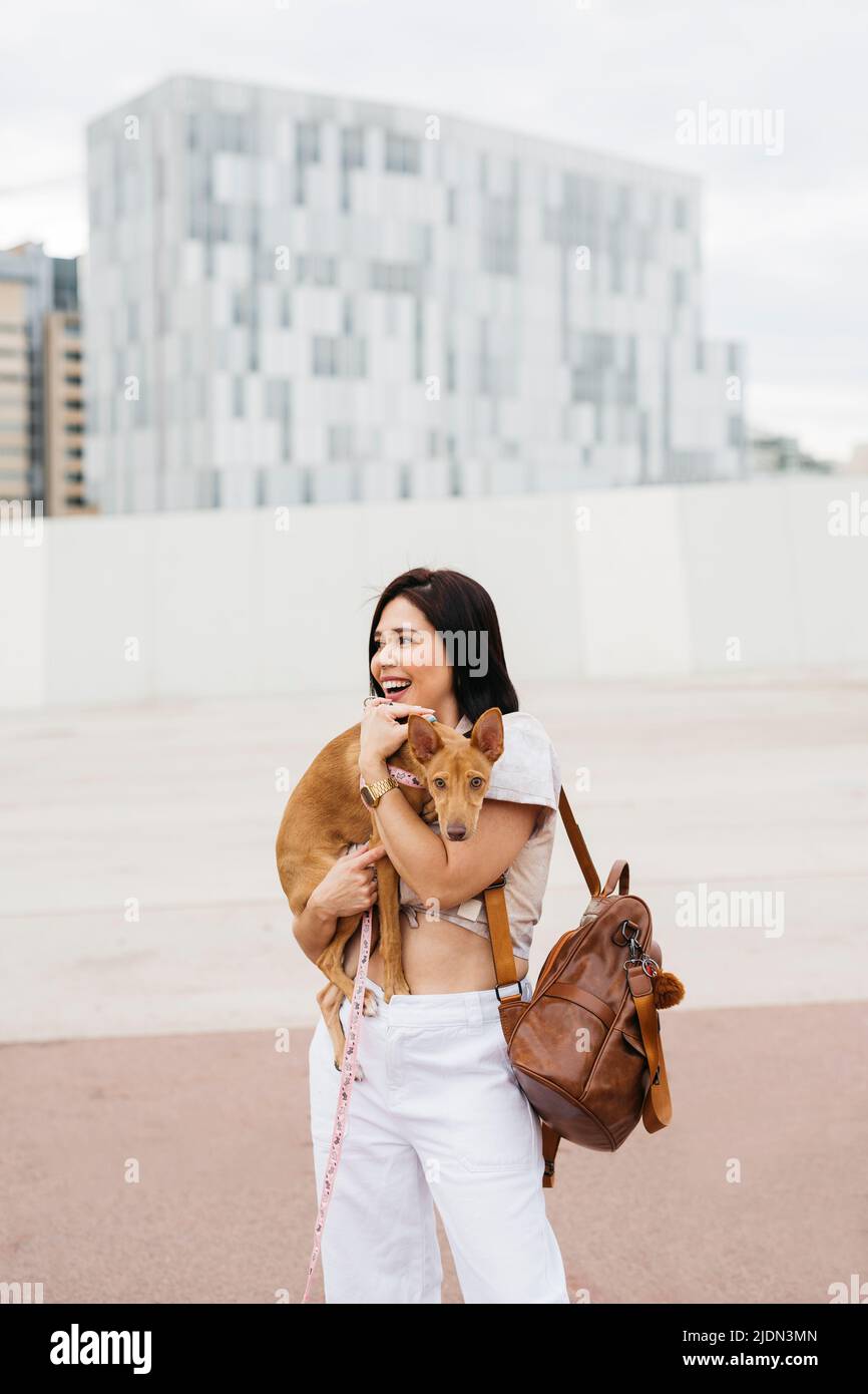 Young woman carrying dog on her arms on the street Stock Photo