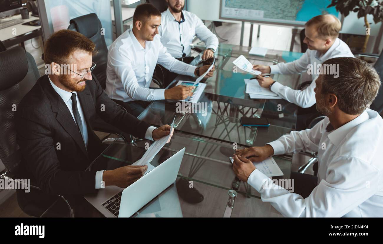 A group of company employees sits at a table in a meeting room. A team