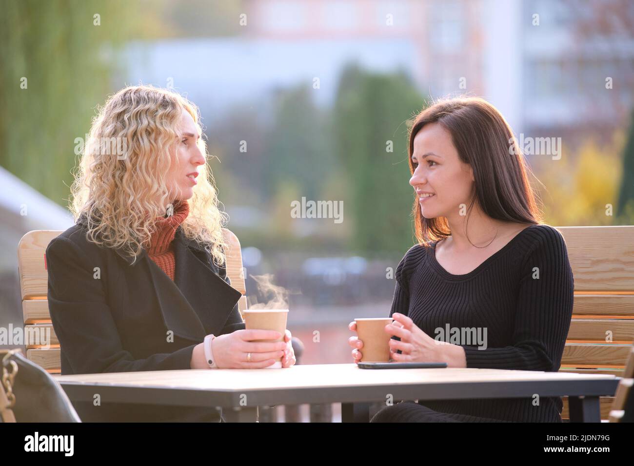 Portrait of two happy young women sitting at city street cafe Stock ...