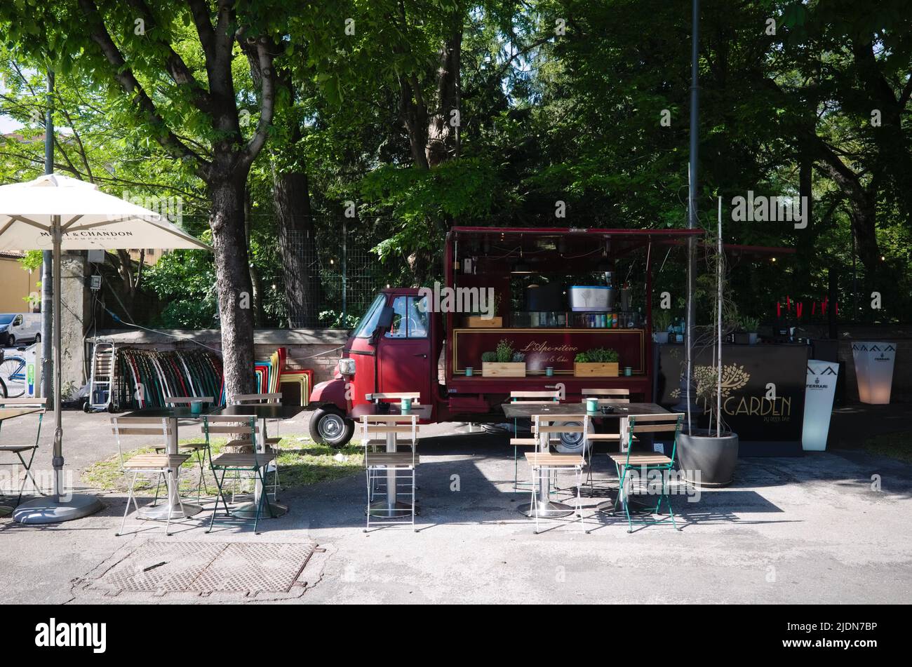 Parma, Italy - May, 2022: Old tuk-tuk converted into small cafeteria with tables and chairs along street. Sidewalk cafe Italian coffee on wheels Stock Photo