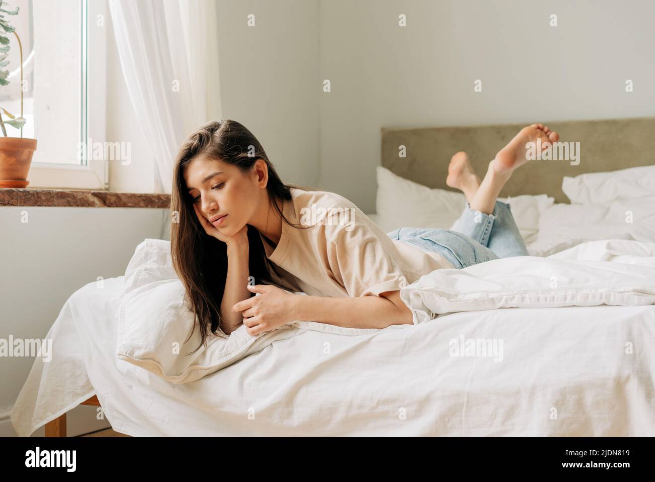 A bored adolescent woman lies on the bed thinking. Stock Photo