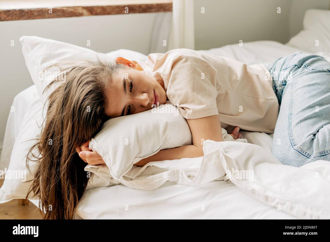 Sad bored young female brunette lies on the bed Stock Photo