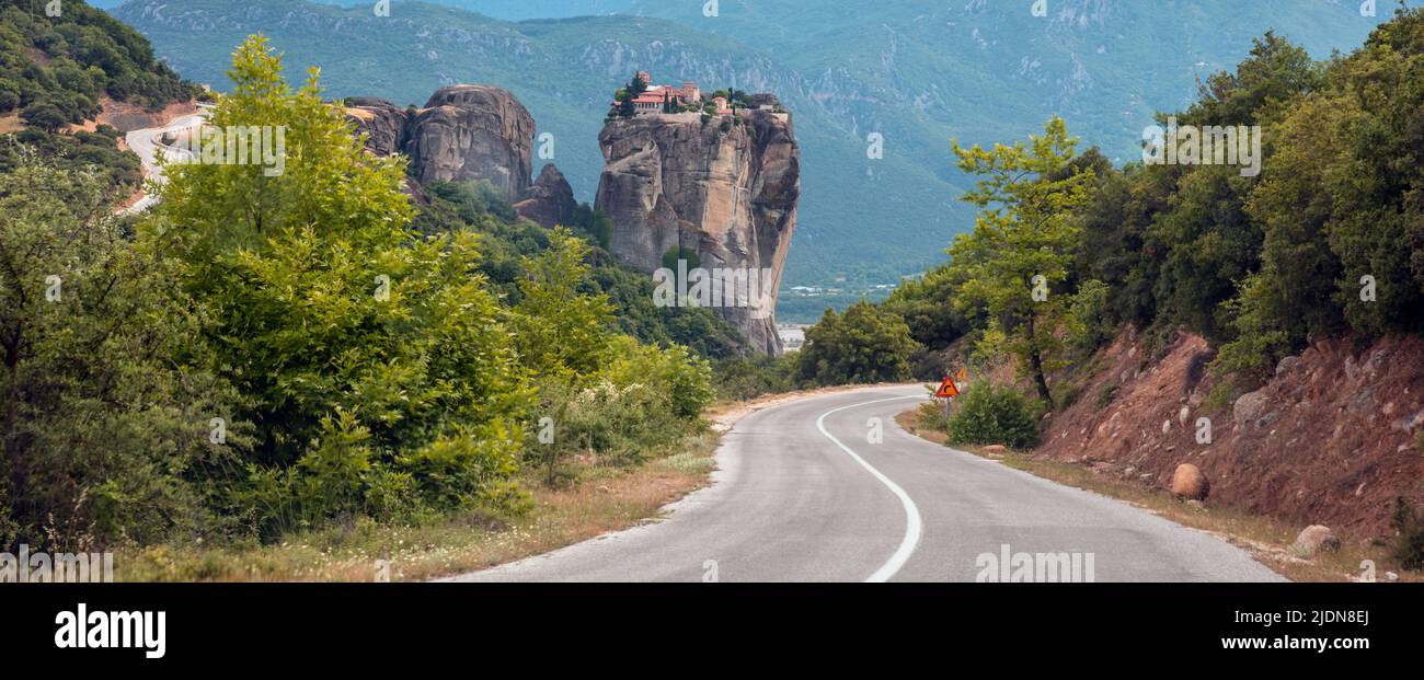 Meteora Greece. Winding asphalt road in the valley. Holy Monastery of Rousanos Saint Barbara buildings on top of rock, Stock Photo