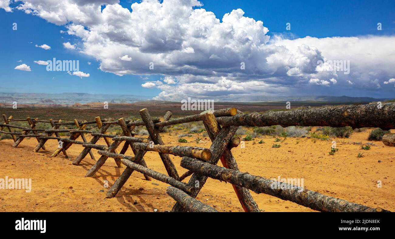 Wood logs fence mark boundaries in a desert landscape, blue sky with clouds. Sunny spring day in Western American countryside, USA Stock Photo
