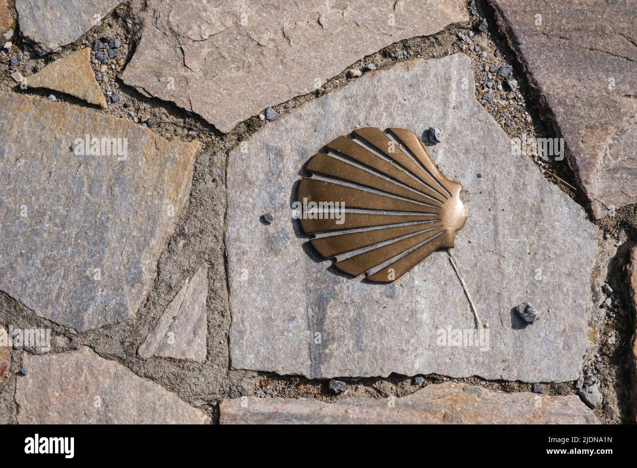 Spain, Cacabelos. Metal Scallop Shell Embedded on Sidewalk Stone Indicates the Direction of the Camino de Santiago.  Castilla y Leon Region. Stock Photo