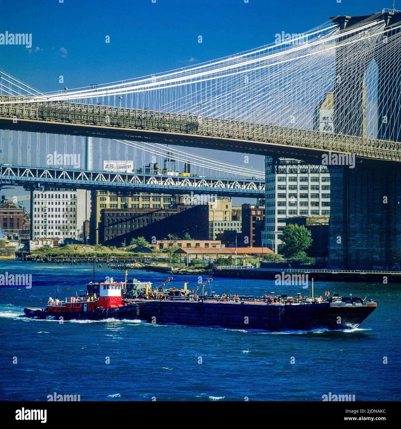 New York 1980s, Brooklyn Bridge, East river, tug boat pushing a barge, New York City, NYC, NY, USA, Stock Photo