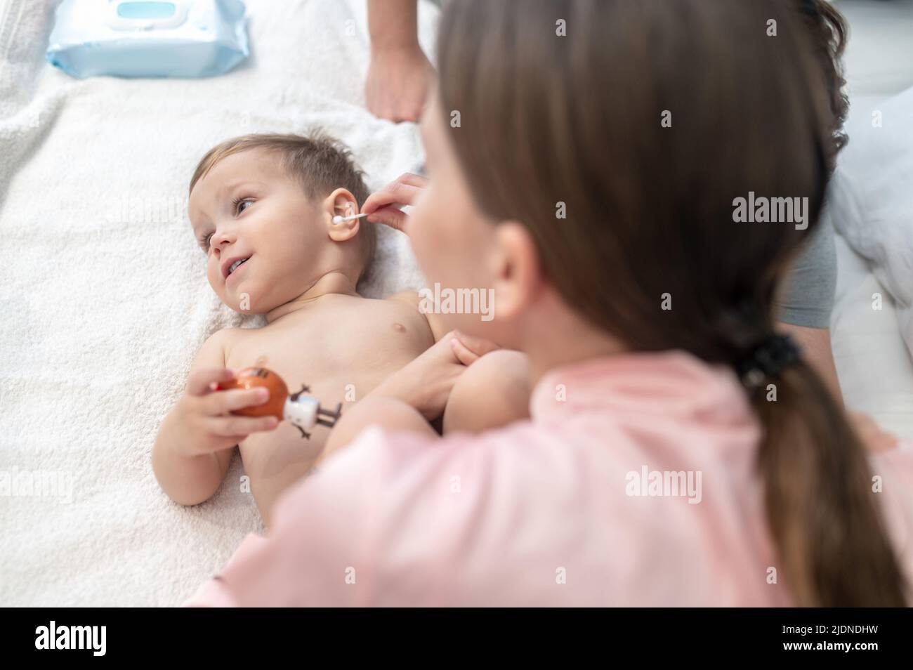 Woman cleaning ear of child lying on bed Stock Photo