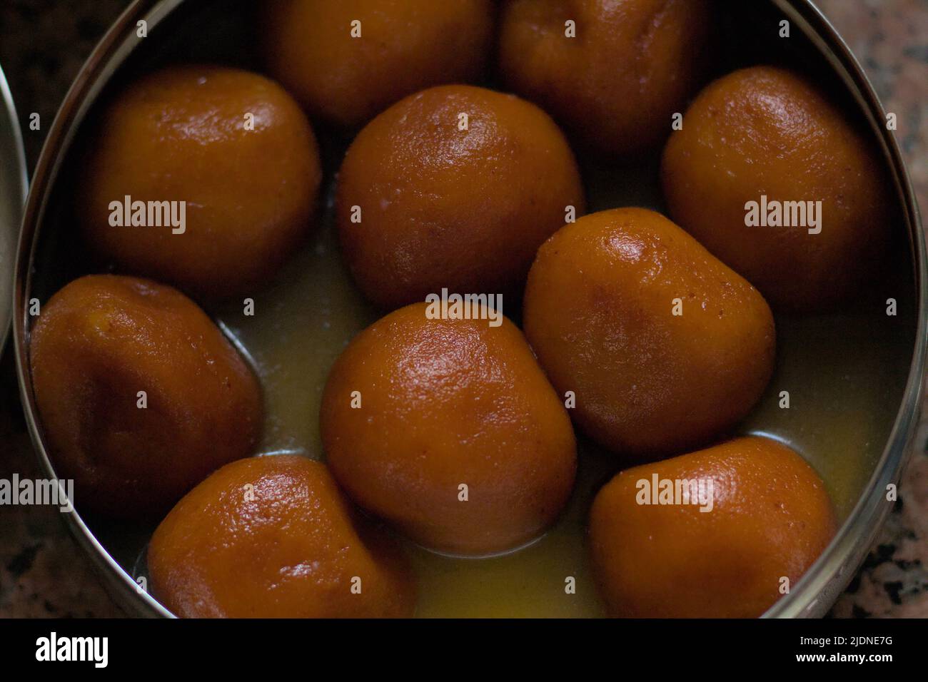 Indian sweets floating in caramel sauce in a steel container Top view. Stock Photo
