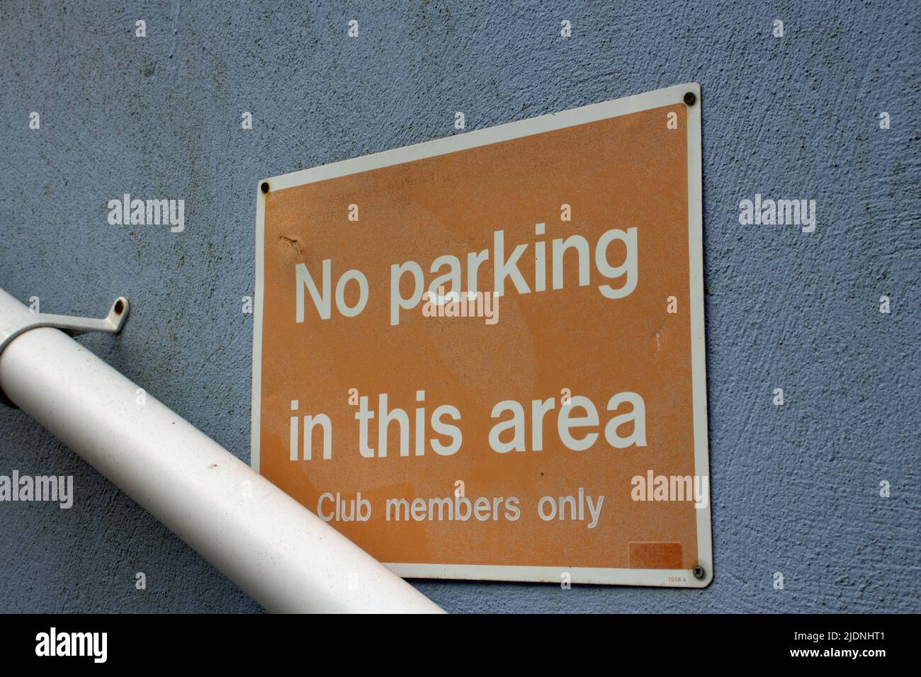 No parking in this area - club members only sign in white letters on an orange background fixed to a cement wall with a drain pipe below Stock Photo