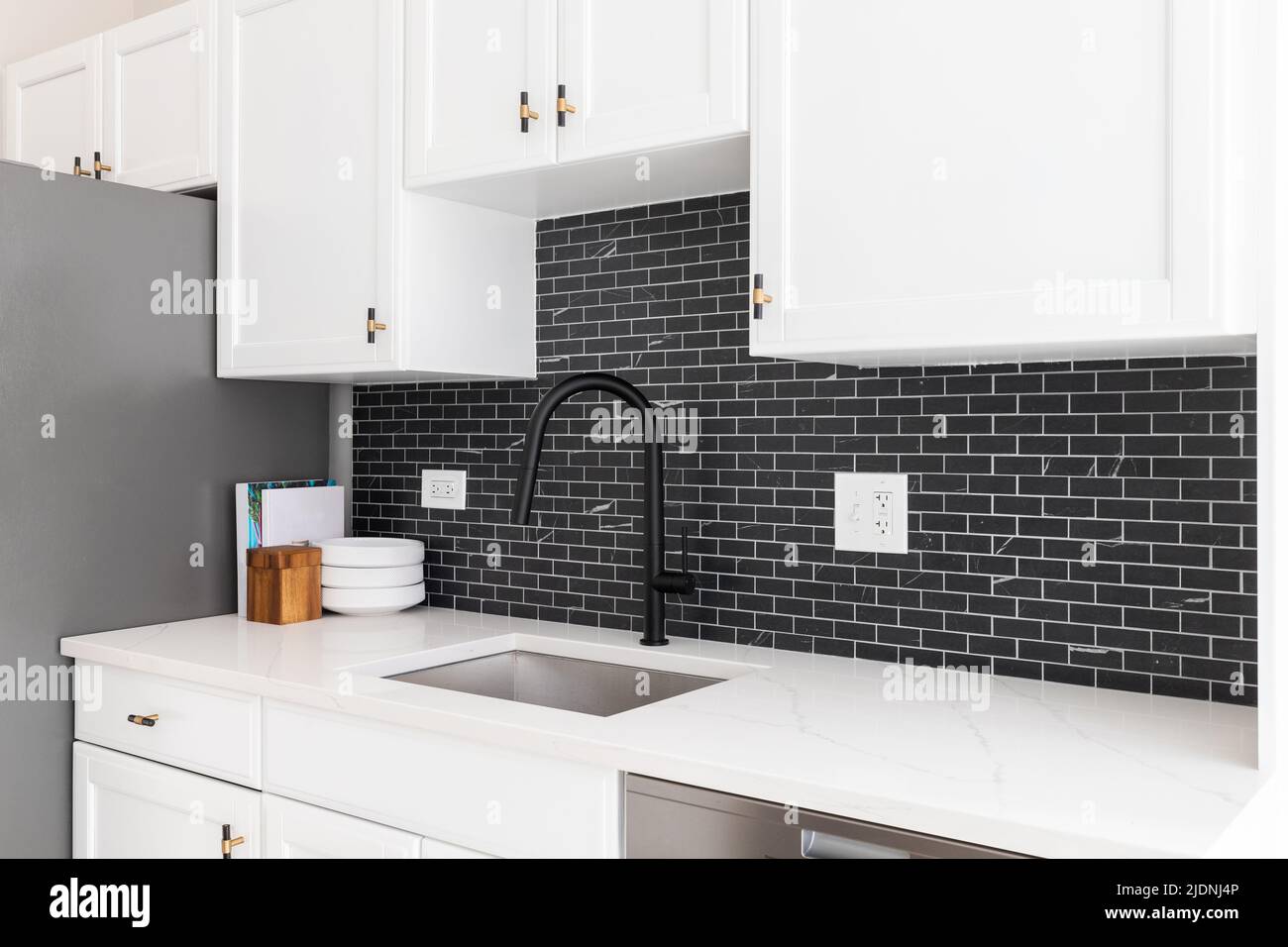 Kitchen sink detail shot with white cabinets, small black marble subway tile backsplash, and a black faucet. Stock Photo