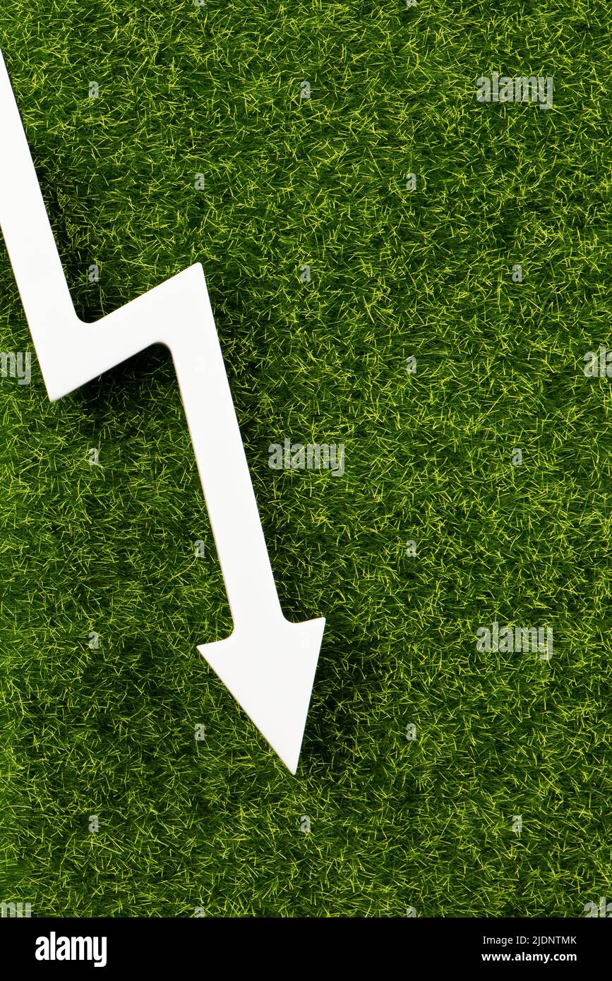 White chart arrow on green grass pointing down. Business loss symbol, ecology concept, green energy spending. Stock Photo