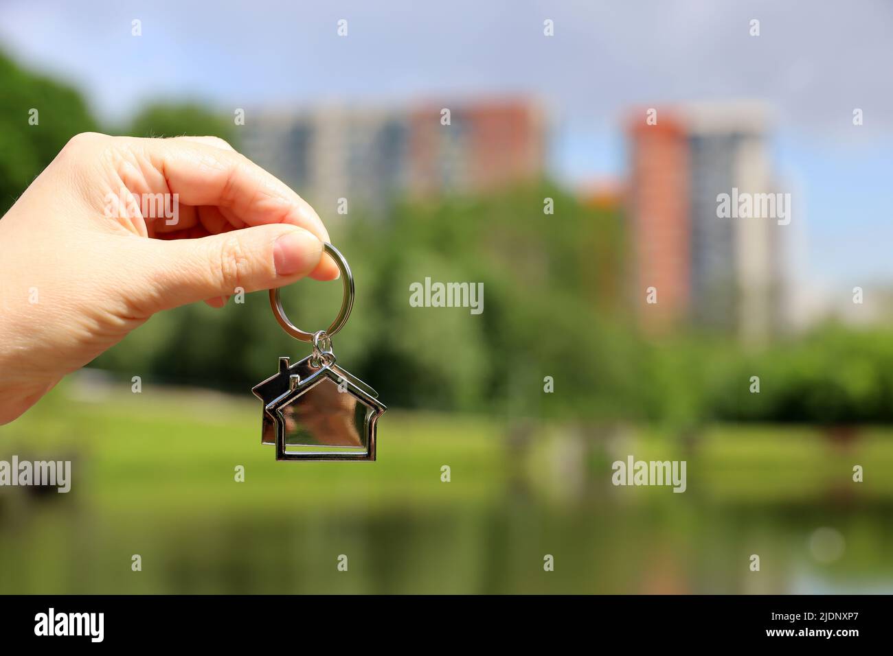Keychain in shape of a house in female hand on background of summer ...