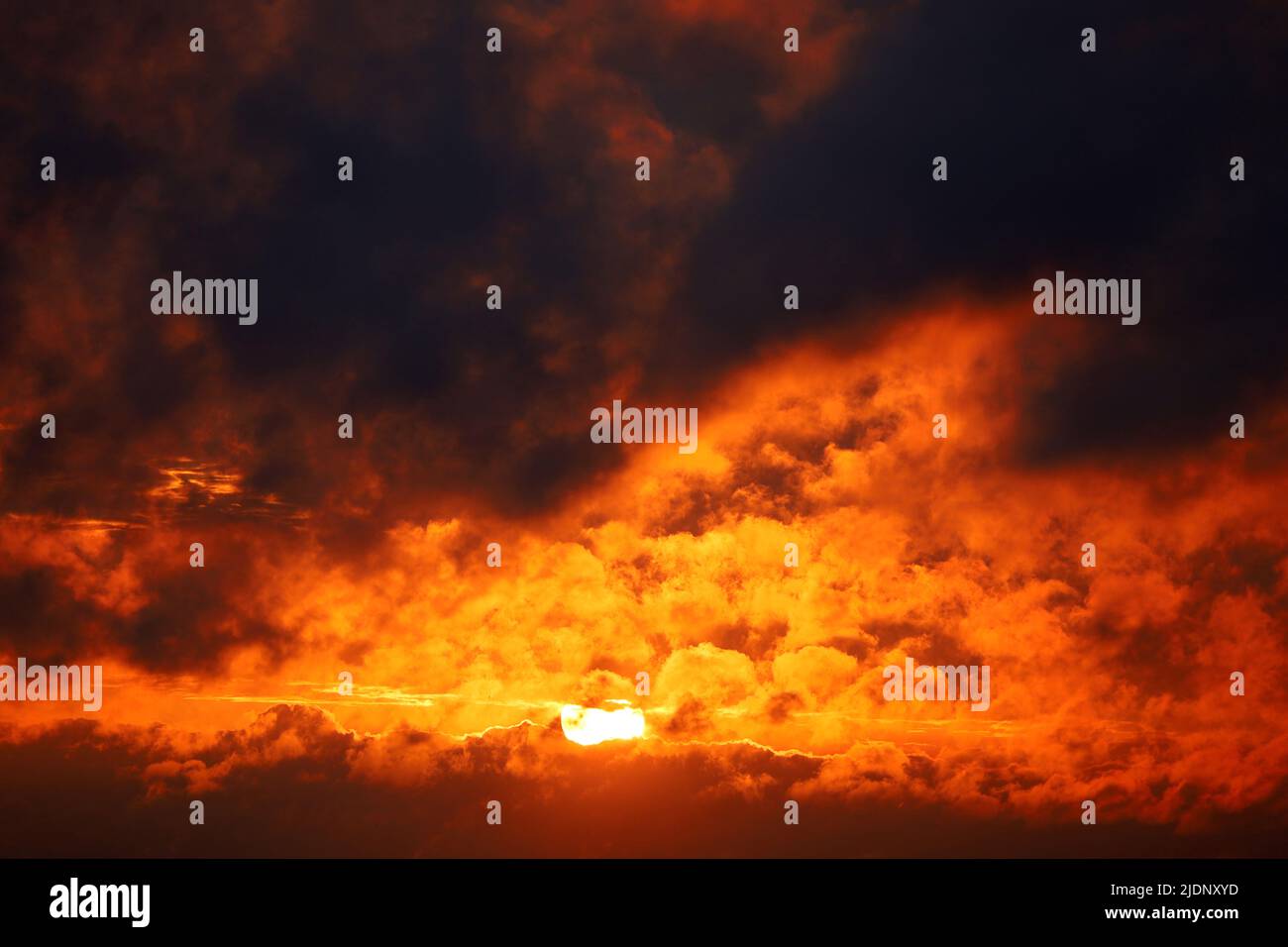 Sunset on dramatic sky, orange sun shining through dark clouds. Picturesque cloudscape for horror background Stock Photo
