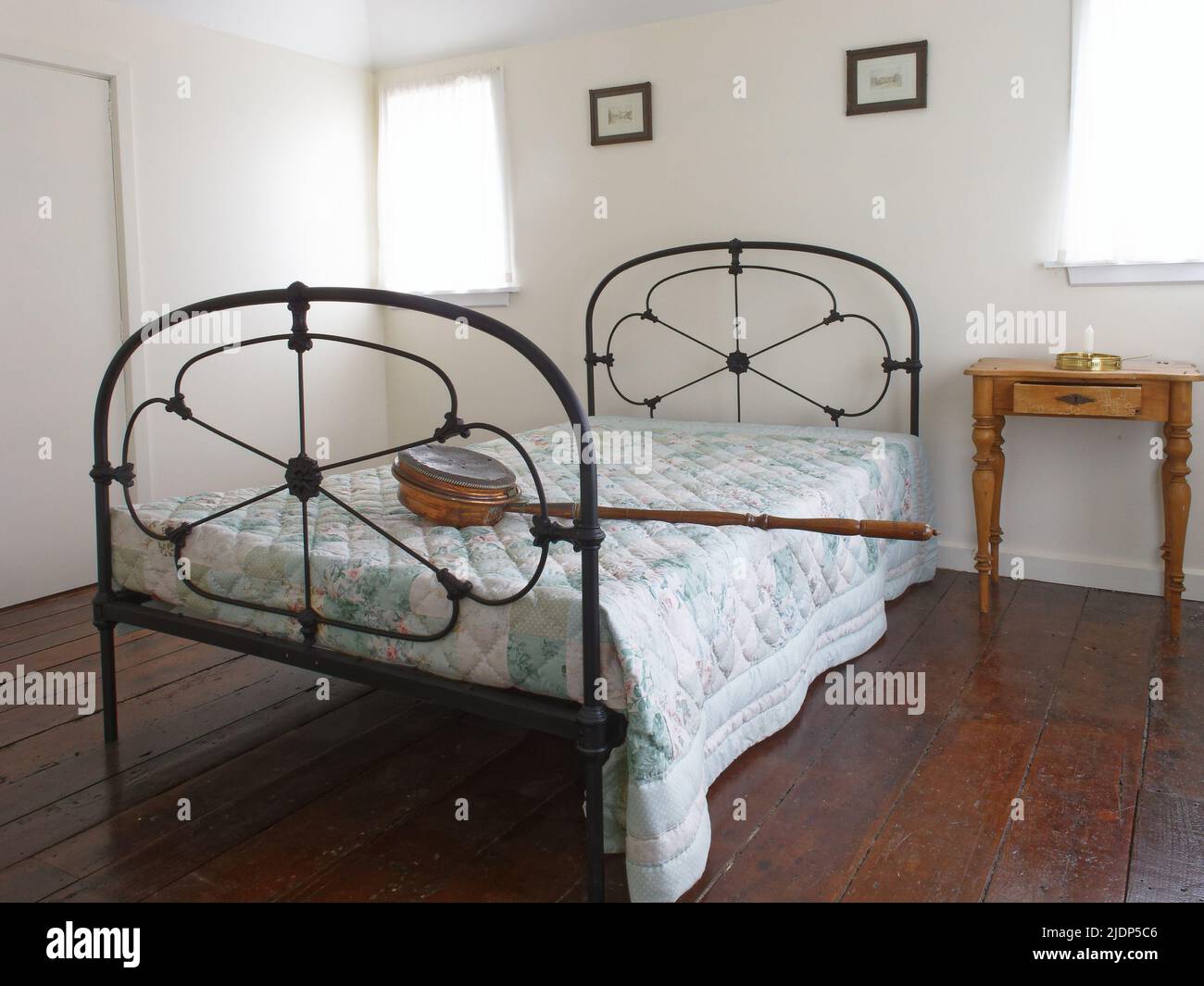 A copper bed warming pan with a long wooden handle lying across a double bed with iron bedstead. Stock Photo
