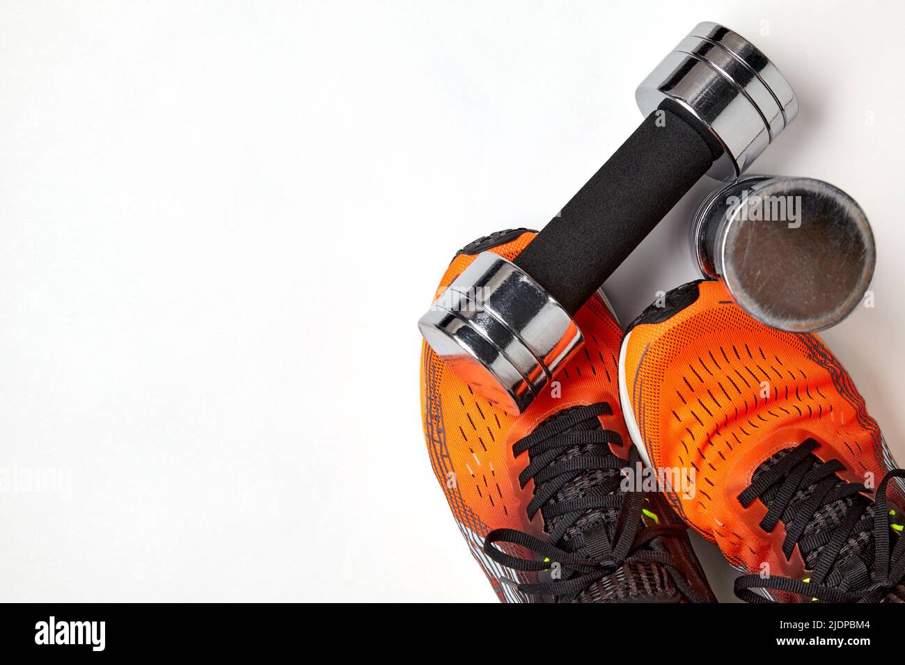 Metallic heavy dumbbell dropped on leg in orange sneaker. Strength