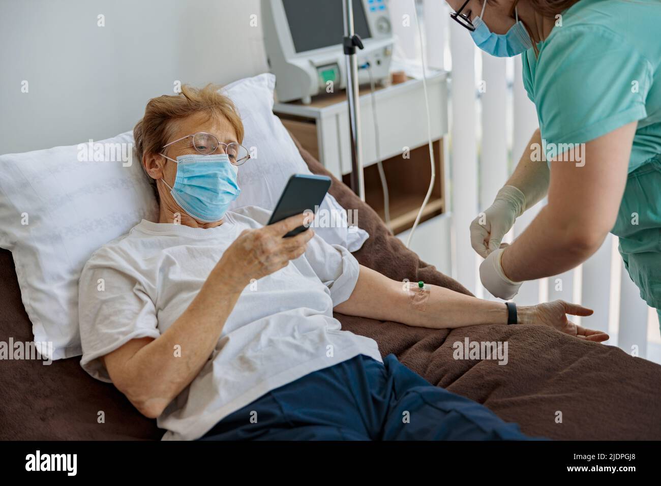 Sick senior patient use phone during medical procedure in hospital ward Stock Photo