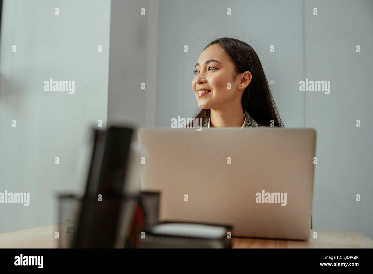 Charming Asian woman working at the office using a laptop looking away ...