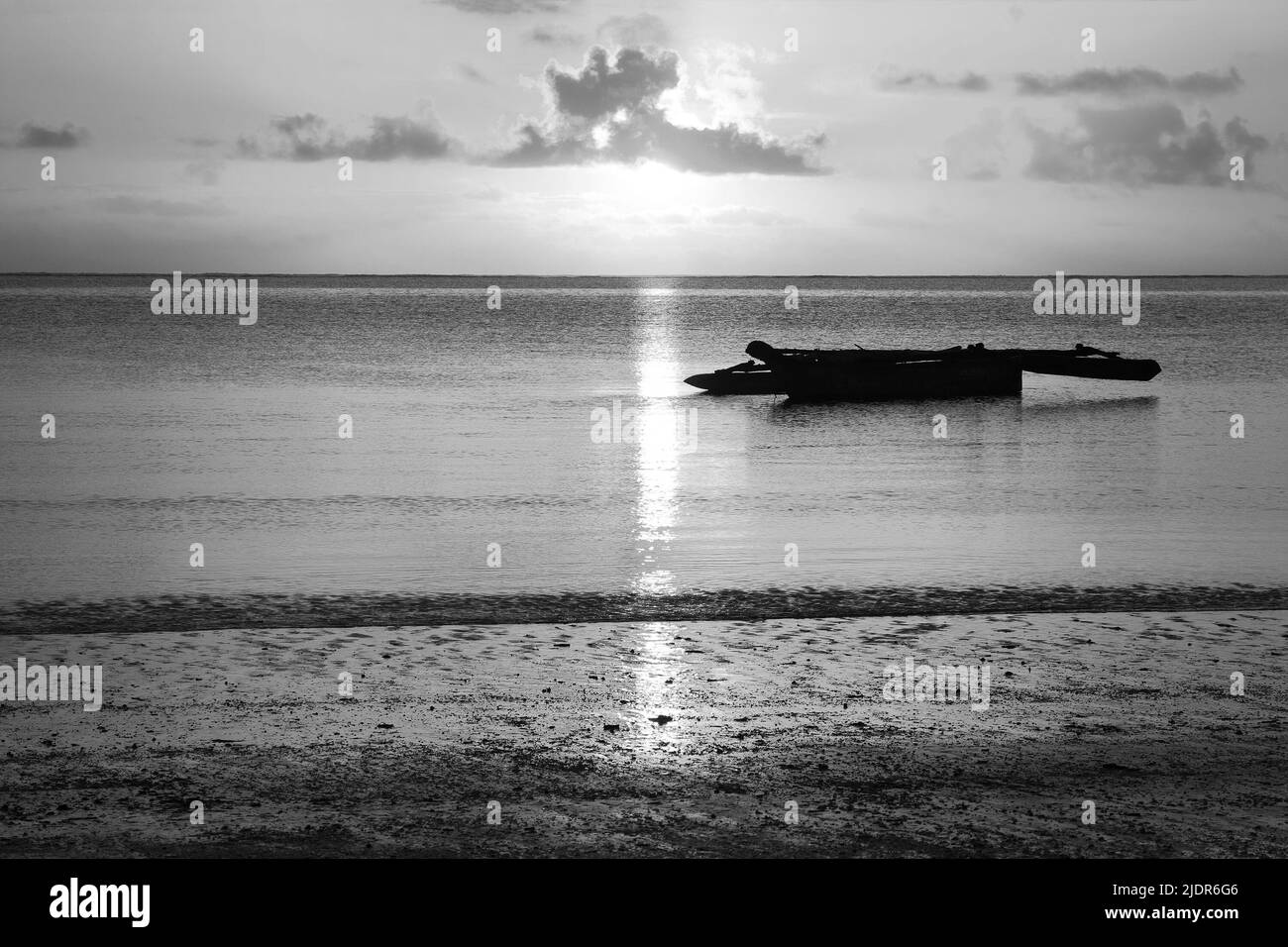 Sunrise at the beach with an African boat (dhow) at the foreground, Zanzibar, Tanzania (black and white) Stock Photo