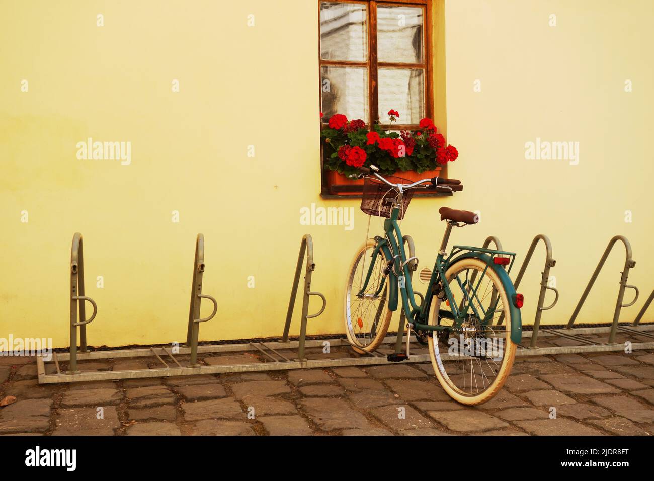 green bicycle parked by a window with red flowers Stock Photo