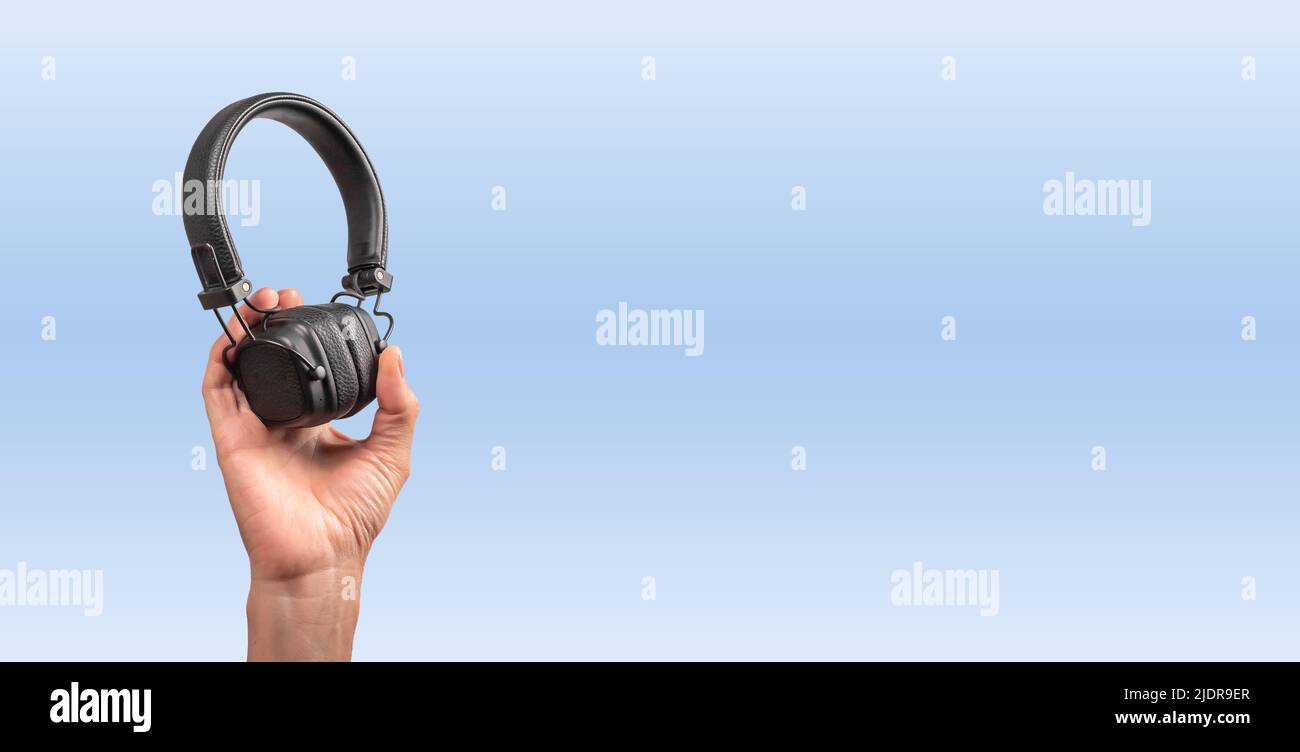 Banner with hand holding wireless headphones on blue background. Cordless device. Place for text. High quality photo Stock Photo