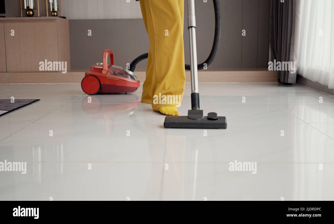 Young girl havig fun while cleaning floor with vacuum cleaner. Happy woman doing housework at home enjoy music wearing earphones. Stock Photo