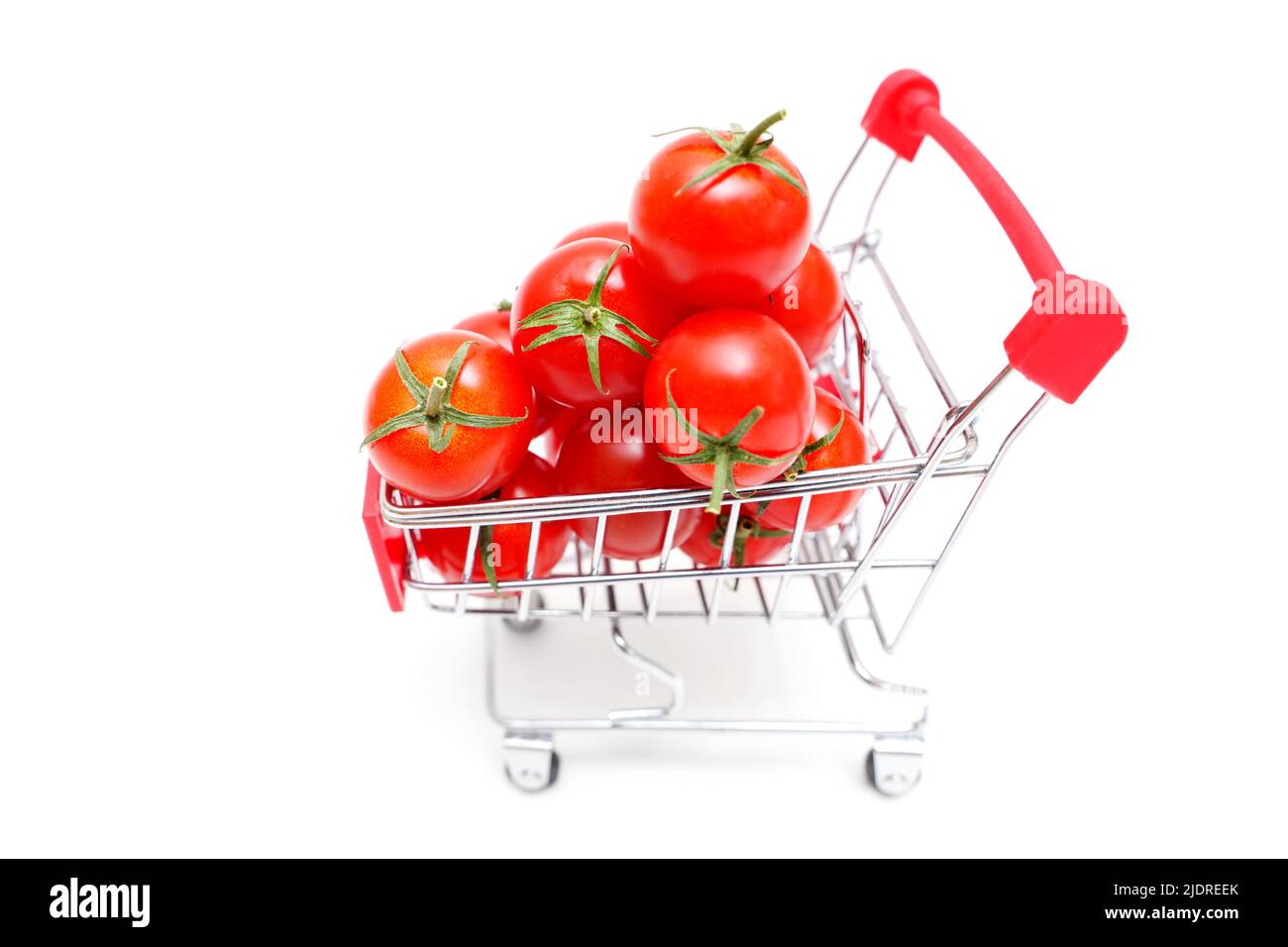 Pile of fresh cherry tomatoes in a miniature shopping trolley isolated on white. Stock Photo