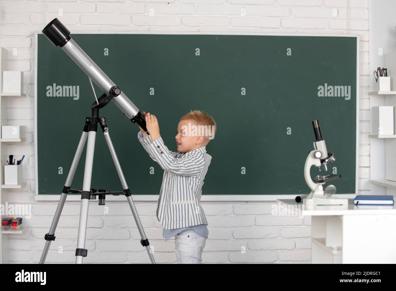 Cute little child with telescope in classroom at elementary school