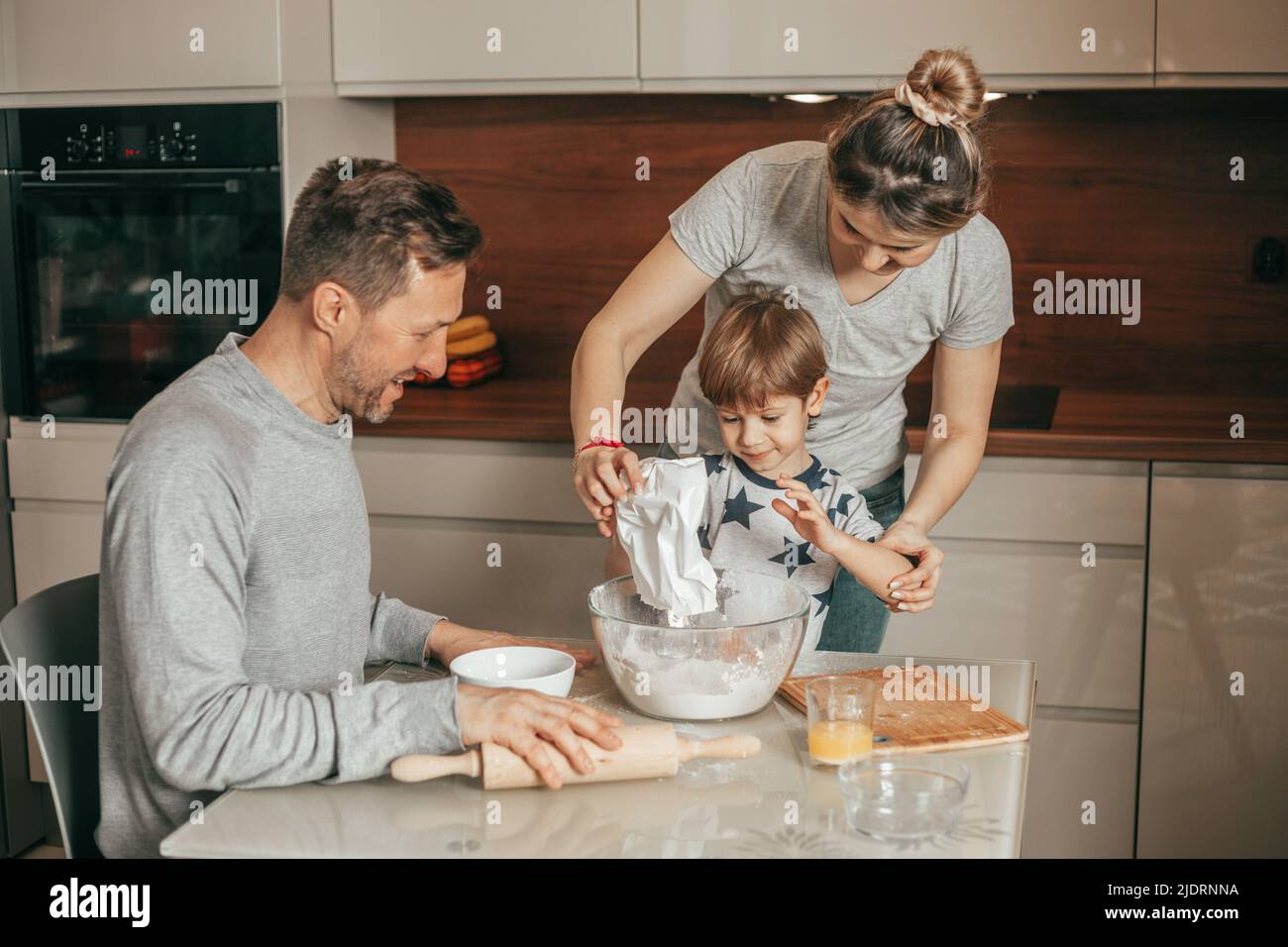 Teamwork. Young family is engaged in baking cookies in kitchen. Teaches Baking lesson for little boy 4-5 years. Son is involved in housework. Stock Photo