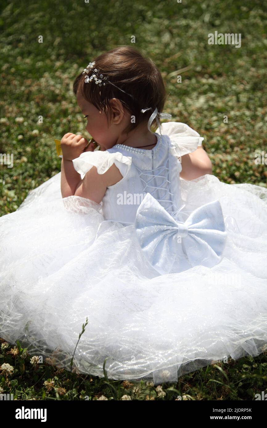 A little girl in a white dress sits on the grass - editorial image ...
